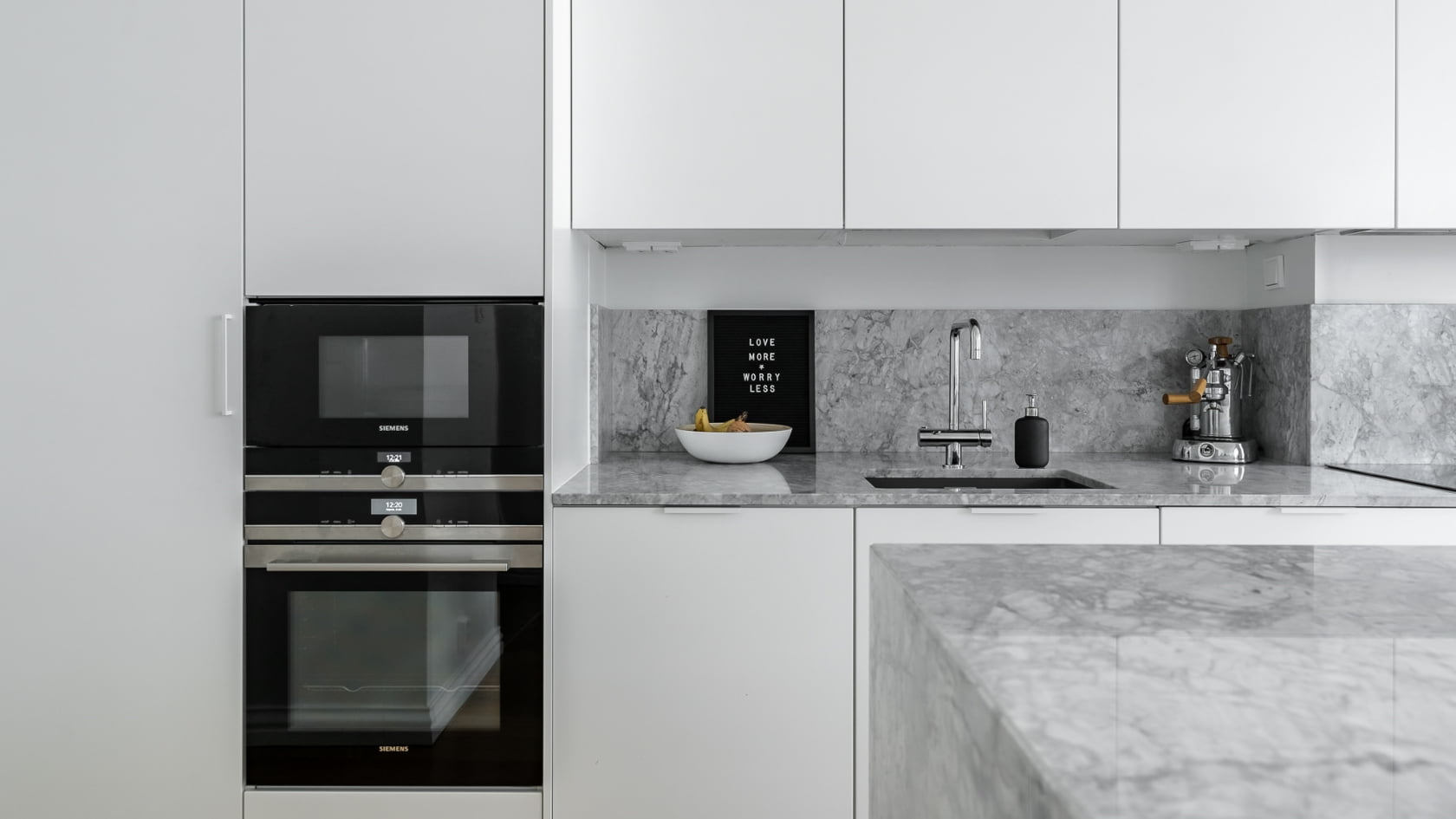 Uuden asunnon keittiö jossa valkoiset kaapit ja marmoritasot